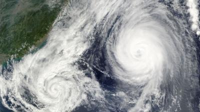 Satellite image of two large cyclones in the ocean near a landmass, with swirling cloud patterns visible.