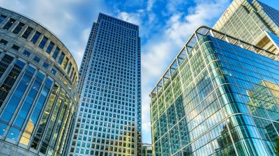 Tall glass skyscrapers under a partly cloudy blue sky, photographed from a low angle, highlighting modern architecture.