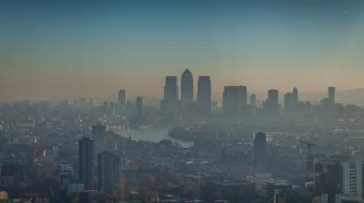 A hazy cityscape with modern high-rise buildings and a river running through the urban area under a blue sky.