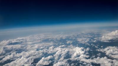 View of white clouds covering the Earth's surface with a gradient blue sky above, taken from a high altitude, possibly from an airplane or stratospheric balloon.