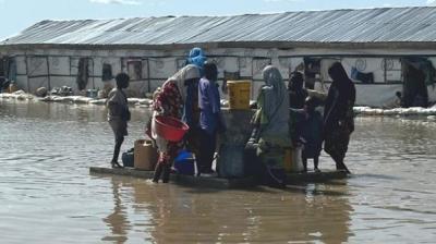 Families wade through floodwaters to access a water point