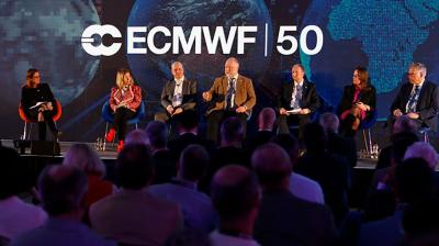 A panel of six people speaks on stage at an ECMWF 50th anniversary event, with an audience seated in front and large screens showing Earth in the background.