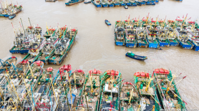 Aerial view of numerous fishing boats tightly clustered together in a harbor with muddy water.