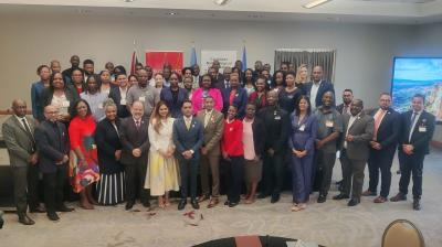 A large group of professionally dressed people pose for a group photo in a conference room, with banners in the background.