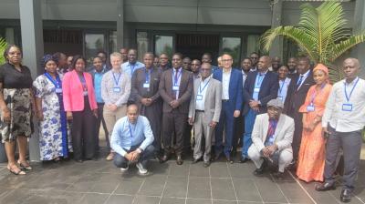 A group of people wearing conference badges pose for a group photo outdoors on a tiled surface, with a building and a potted plant in the background.