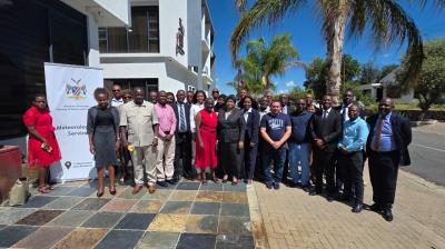 A large group of people posing for a group photo outdoors in front of a building with a banner reading "Meteorological Services.