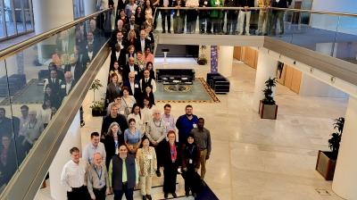 A large group of people poses for a group photo in a modern building with two floors, some standing on the upper level and others on the ground floor.
