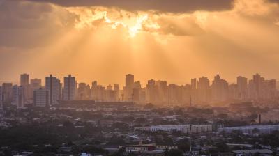 Sun rays break through clouds over a city skyline with high-rise buildings, casting a warm golden light on the urban landscape below.