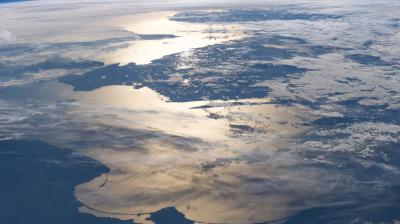 A view of northwestern Europe from space, with land, clouds, and sunlight reflecting off the surrounding sea.