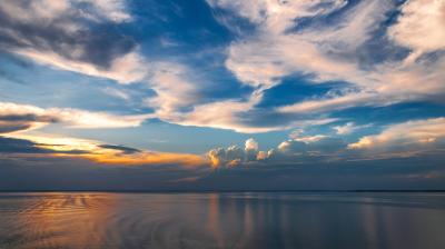 Calm water reflects a colorful sky with scattered clouds at sunset, creating a peaceful and open landscape.