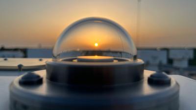 : Close-up of an atmospheric monitoring instrument at sunset, with the sun visible through its transparent dome.