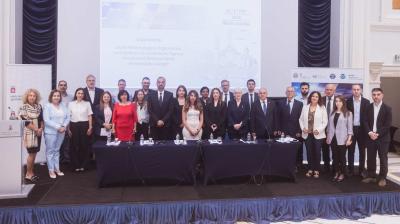 A group of about 25 people in business attire pose for a photo in a conference room in front of a screen displaying meeting details.