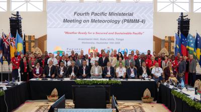 A large group of people poses for a photo at the Fourth Pacific Ministerial Meeting on Meteorology, with national flags and a conference banner in the background.