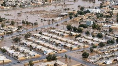 Aerial view of a town affected by flooding, with water covering streets and partially submerging buildings; desert landscape in the background.