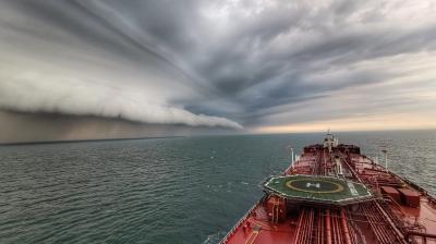 A ship sails on the ocean toward a distant rolling cloud beneath a dramatic, stormy sky.