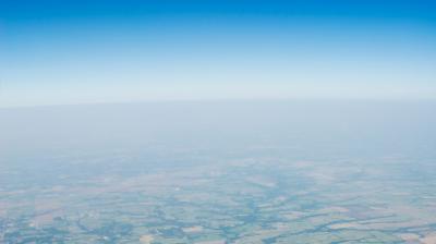 Aerial view of farmland with a clear blue sky above and a hazy horizon in the distance.