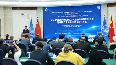 A conference room with delegates seated, facing speakers at a podium under banners for a WMO climate event in Beijing. Chinese and UN flags are displayed behind the speakers.