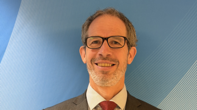 John-Harding headshot with glasses, a salt-and-pepper beard, and a suit and tie smiling at the camera.