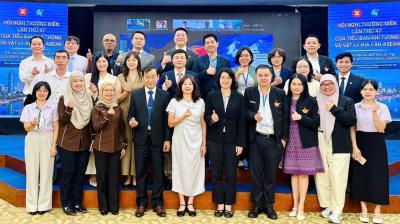 A large group of people in business attire posing for a photo on a stage in front of a digital screen displaying text about an ASEAN meeting.
