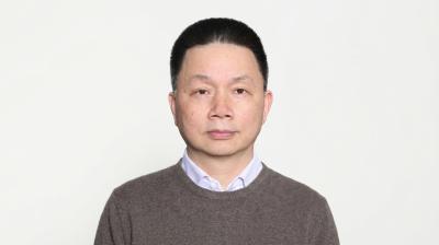 A middle-aged man with short dark hair, wearing a brown sweater over a collared shirt.