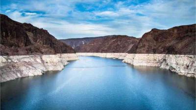 A large reservoir with receding water levels, surrounded by rocky cliffs showing a visible white mineral line along the shoreline under a partly cloudy sky.