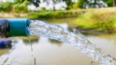 A blue pipe releases a stream of clear water into a pond or small body of water, with green vegetation visible in the background.