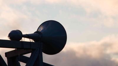 A large outdoor loudspeaker is mounted on a wooden structure against a cloudy sky at dusk.