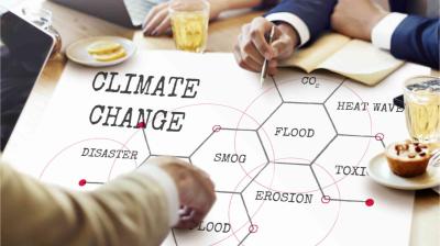 People discuss a chart about climate change impacts, showing keywords like disaster, smog, erosion, flood, CO2, heat wave, and toxic, with drinks and laptops on the table.