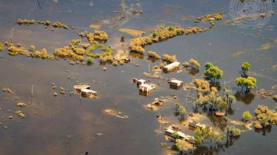 Aerial view of a flooded rural area with partially submerged houses, trees, and vegetation scattered throughout the water.