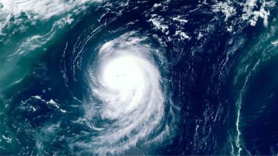 Satellite image shows a large hurricane swirling over the ocean, with a well-defined eye at the center and spiral cloud bands extending outward.