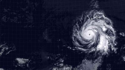 Satellite image shows a large hurricane with a well-defined eye swirling over the ocean, surrounded by cloud bands and clear grid lines marking coordinates.