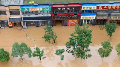 Floodwater partially submerges trees and engulfs the ground floor of several storefronts in a commercial area.