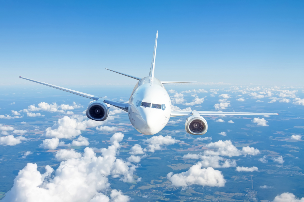 A passenger airplane flying above the clouds against a blue sky.