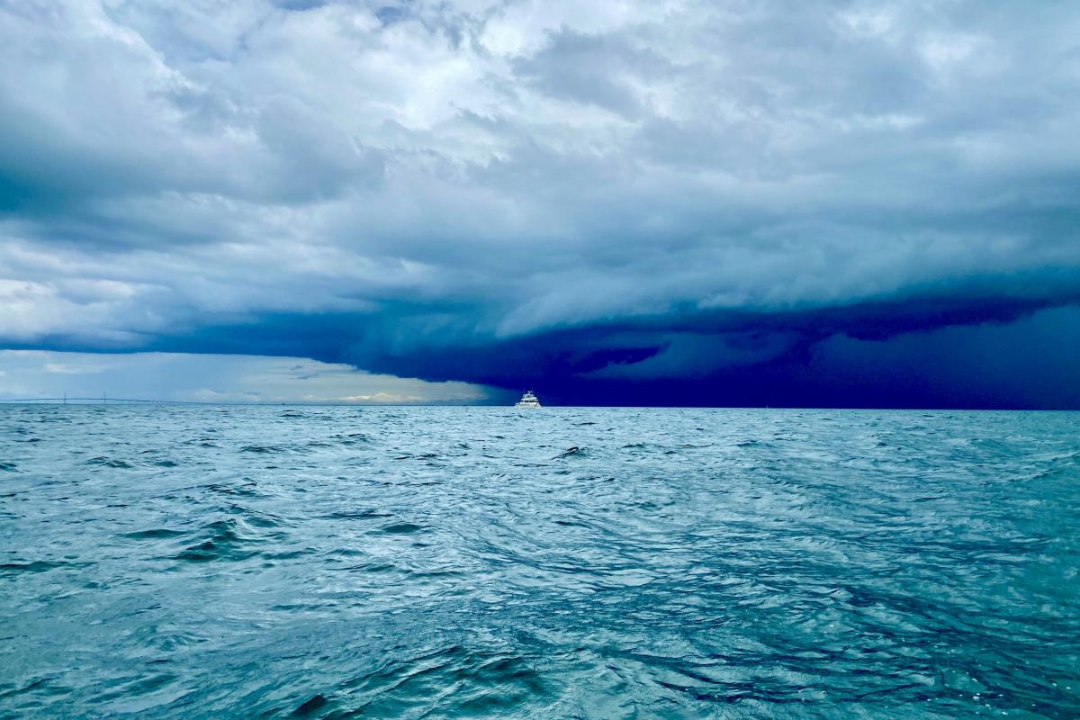 A boat is visible on the horizon under a dark, stormy sky, with choppy blue water in the foreground.