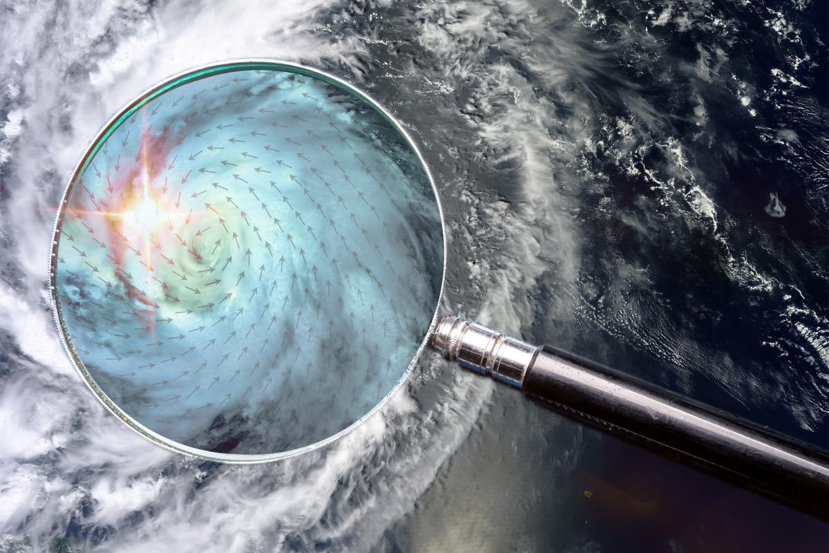 A magnifying glass is held over a satellite image of a hurricane, enlarging the storm's swirling center and highlighting wind patterns.