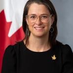 A woman with glasses in front of a canadian flag.
