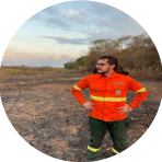 A man in an orange jacket standing in a burned field.