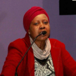 A woman in a red turban speaking into a microphone.