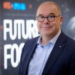 A man in a suit and glasses stands in front of a backdrop with the words "Future Focus" visible.