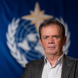 Lars Peter Riishojgaard standing in front of WMO flag.