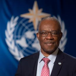 Yinka R. Adebayo standing in front of WMO flag.
