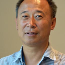 Toeb Karma in a striped shirt standing in front of a room.