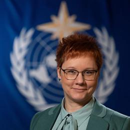 A woman with glasses standing in front of a flag.