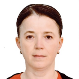 A woman with fair skin and dark brown hair pulled back, wearing small hoop earrings, a red top, and a black sweater, facing the camera against a plain white background.