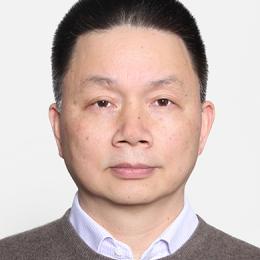 A middle-aged man with short, dark hair, wearing a gray sweater over a collared shirt, is facing the camera against a plain white background.