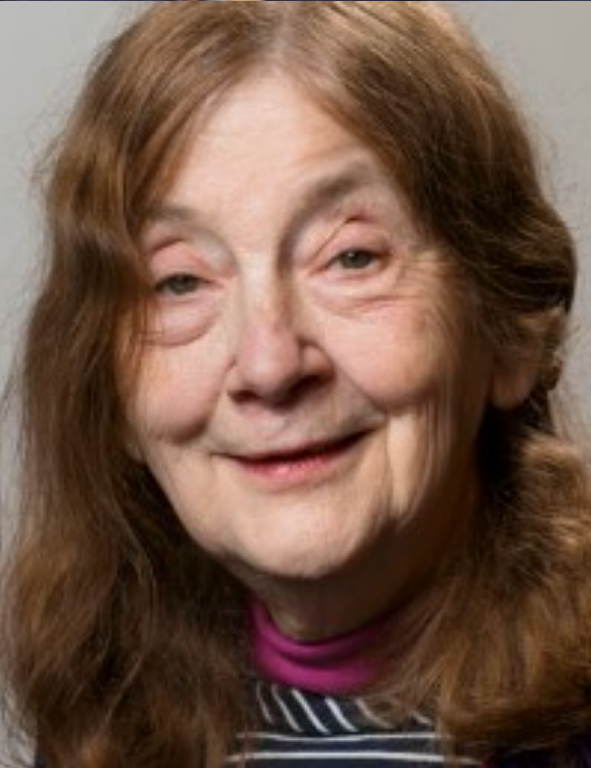 An older woman with long hair and a purple shirt.