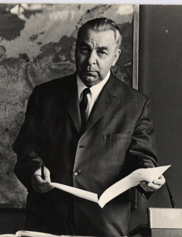 A man in a suit standing in front of a map.