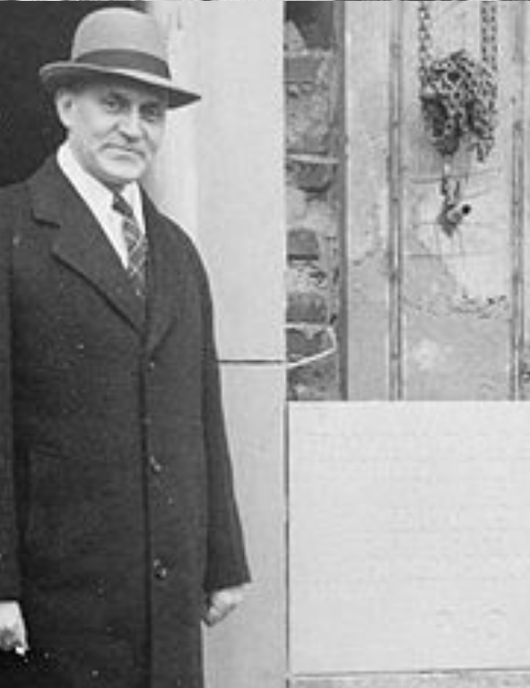 A man in a coat and hat standing in front of a door.