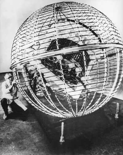 A man kneeling in front of a large metal sphere.