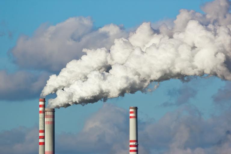 Industrial smokestacks emitting large plumes of white smoke against a blue sky with clouds.